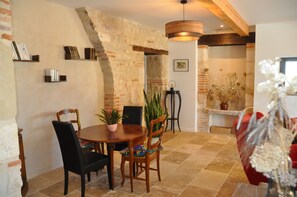 Un coin repas avec un mur en briques, une table en bois et des chaises. On y trouve également des étagères et une plante en pot.