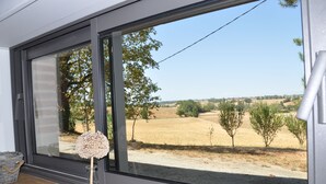 Une pièce dotée d’une grande fenêtre donnant sur un paysage rural, avec des champs et des arbres.