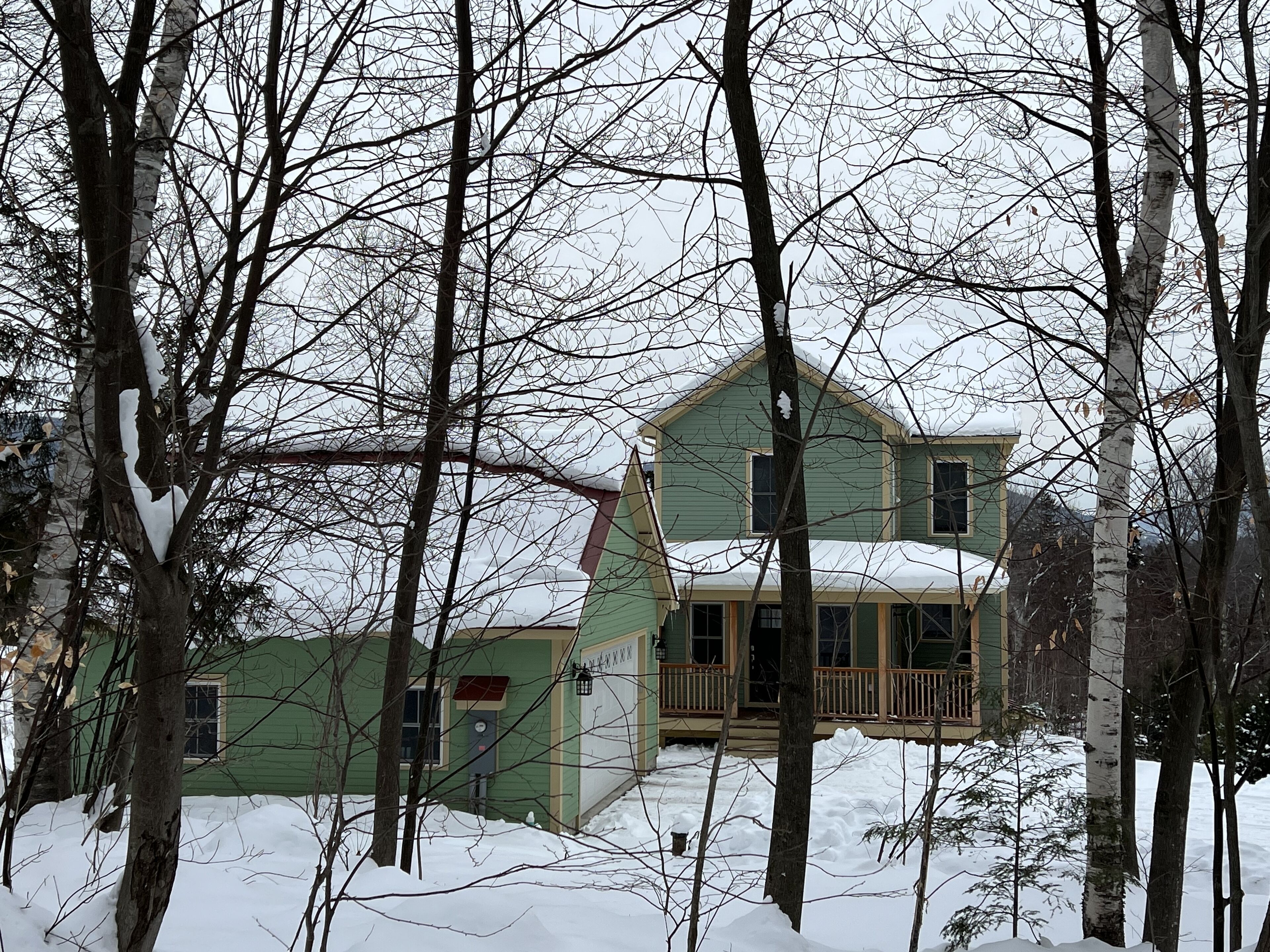 A two-story house with a porch, surrounded by snow-covered trees.