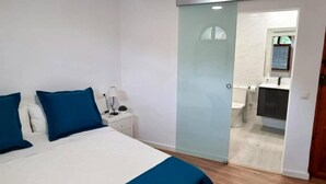 A bedroom with a bed, nightstands, a desk, and a sliding door leading to a bathroom. - Tourist House in the center of Vilafamés (Vilafamés)