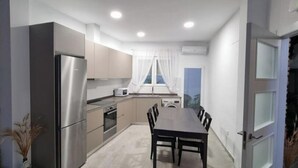A modern kitchen with a dining table and chairs, a refrigerator, oven, microwave, and a window with curtains. - Tourist House in the center of Vilafamés (Vilafamés)