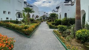 A pathway flanked by white buildings with balconies, surrounded by well-maintained gardens and palm trees. - La Vida Villa Alcudia Simr-Fnideq (Fnideq)