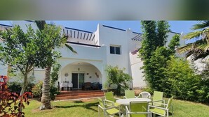 A white building with a covered patio, a small table, and green chairs. - La Vida Villa Alcudia Simr-Fnideq (Fnideq)