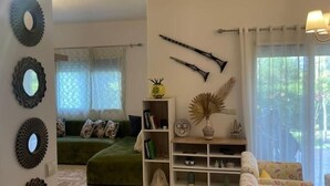 A living room with a green sofa, a patterned armchair, a bookshelf, decorative mirrors, and a window with curtains. - La Vida Villa Alcudia Simr-Fnideq (Fnideq)