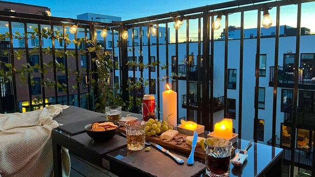 Un balcón con una mesa preparada para una comida, incluyendo una vela, bebidas y aperitivos.