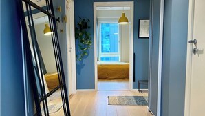 Un pasillo con piso de madera, un espejo grande y vista a una habitación con cama y ventana.