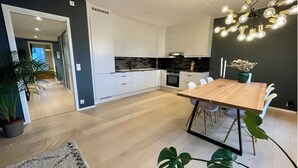 Una cocina moderna con armarios blancos, salpicadero negro y una mesa de comedor de madera con sillas blancas.