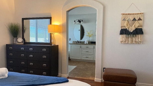 A bedroom with a bed, dresser, and a mirror. There is a hallway leading to a bathroom. - Purified pool-private back yard-family  (Tucson)