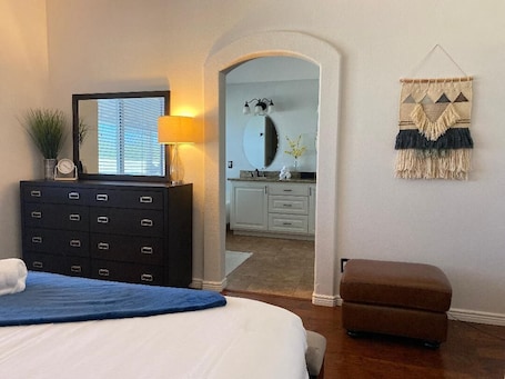 A bedroom with a bed, dresser, and a mirror. There is a hallway leading to a bathroom.