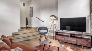 A modern living room with a staircase, a flat-screen TV, a sofa, a chair, and a lamp. - Modern-Industrial 2B Townhouse Close to DT! (Jacksonville)