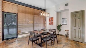 A dining area with a large table, chairs, a hanging light fixture, and a sliding glass door. - Modern-Industrial 2B Townhouse Close to DT! (Jacksonville)