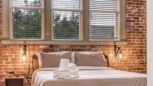 A bed with a headboard, a window with blinds, and a brick wall. - Modern-Industrial 2B Townhouse Close to DT! (Jacksonville)