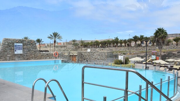 Une piscine aux murs en pierre, avec des palmiers en arrière-plan.