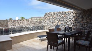 Une terrasse aux murs en pierre, une table avec des chaises et une vue sur le paysage environnant.