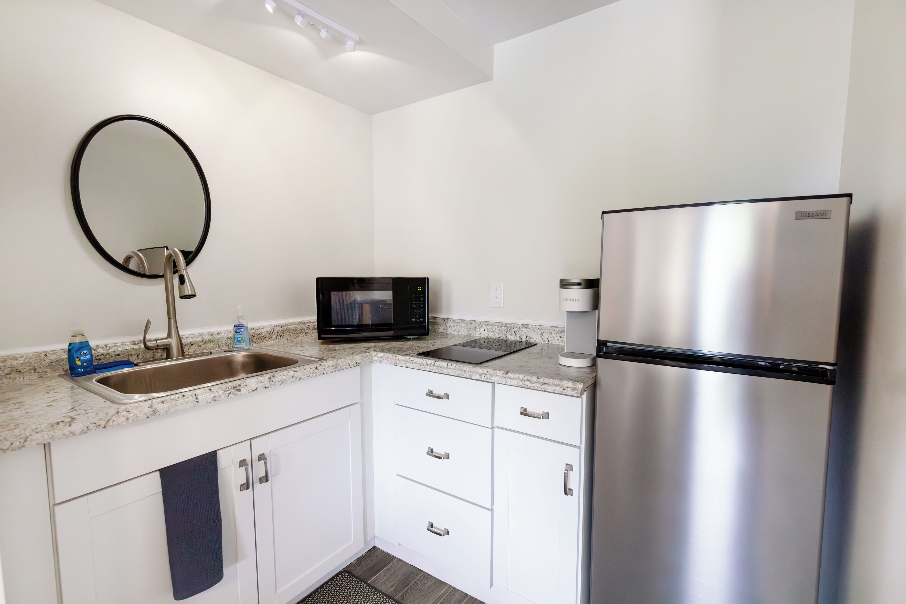 Una cocina moderna con armarios blancos, un refrigerador de acero inoxidable, un microondas y un lavabo con grifo.