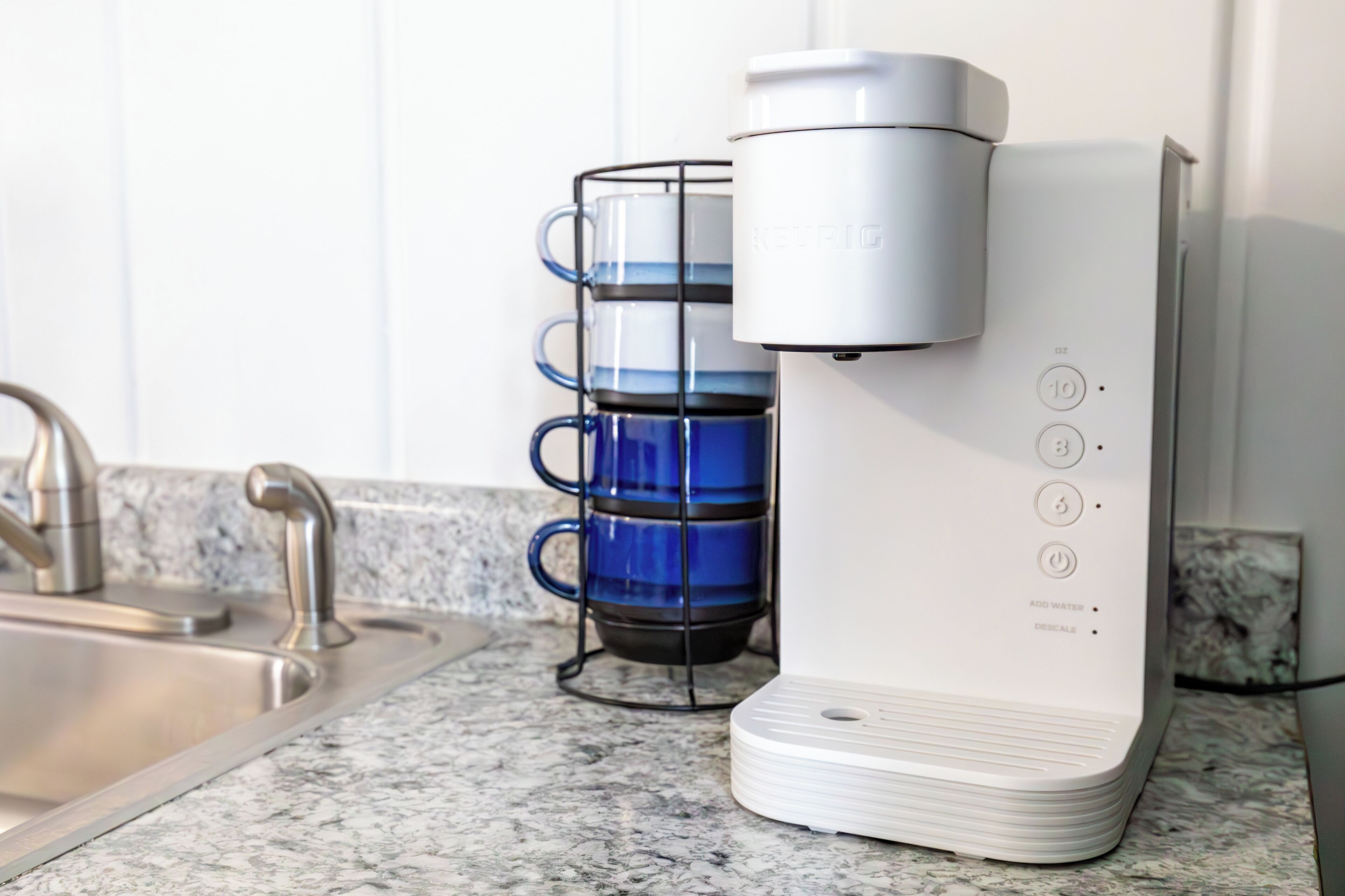 A kitchen with a coffee maker, a sink, and a blue mug holder.