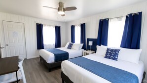 A hotel room with two beds, a desk, and a ceiling fan.