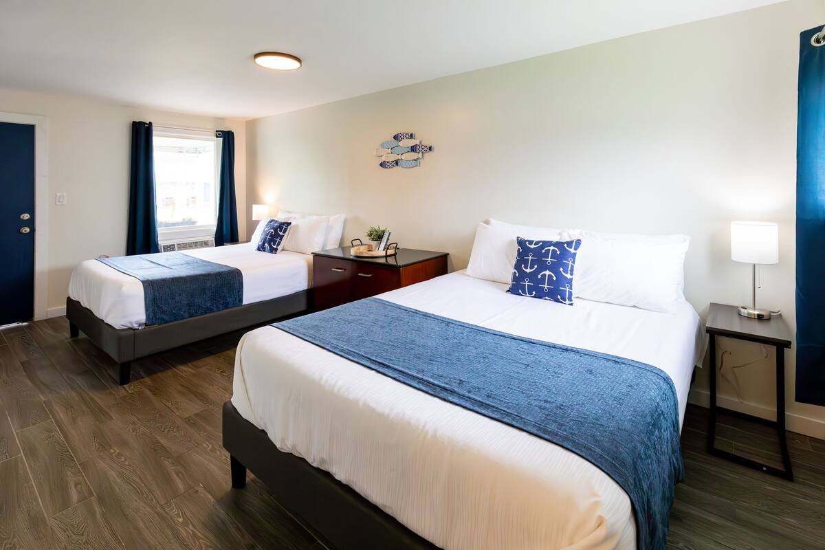 A hotel room with two beds, a small table, and a nightstand.