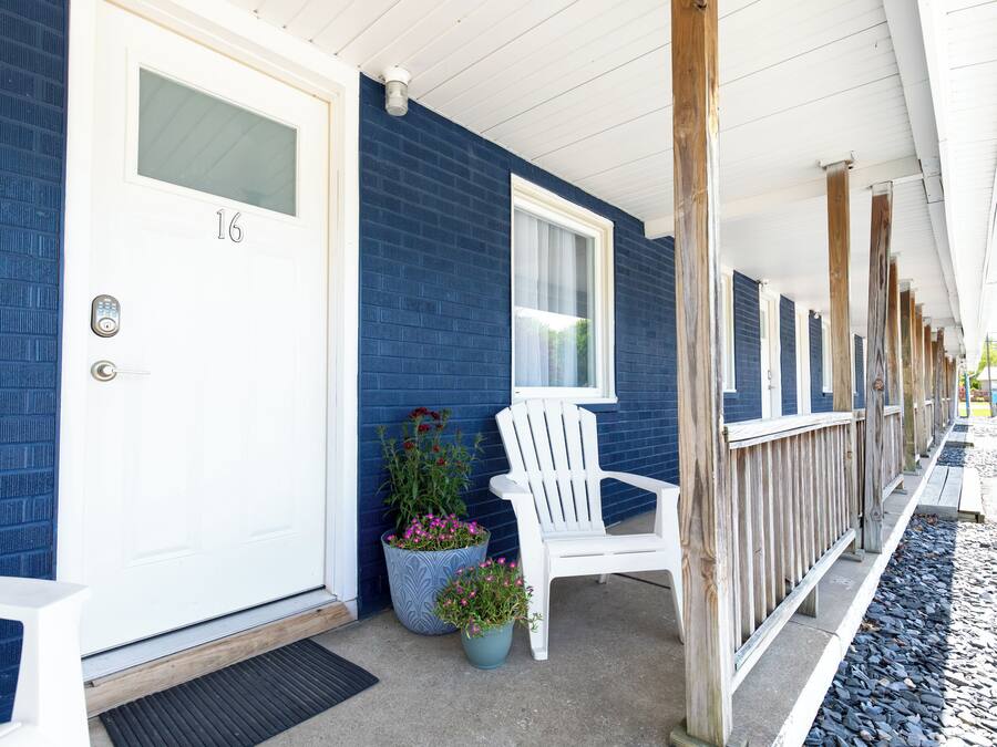 A row of white-framed windows, a white door with a number, and a white chair on a porch with blue walls.