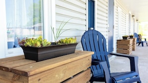A wooden bench and a blue chair outside a house with white siding and a blue door.
