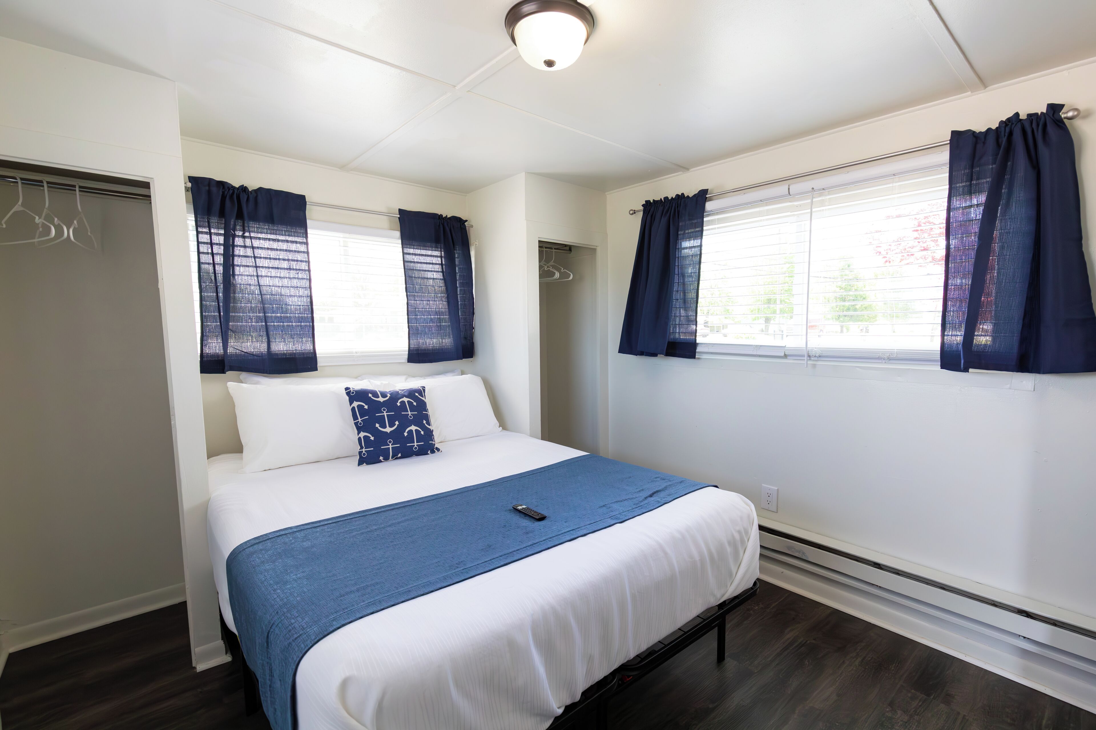 Un dormitorio con cama, mesita de noche, ventana con cortinas, armario y luz en el techo.