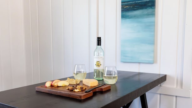 A table with a bottle of wine, glasses, cheese, and fruit.