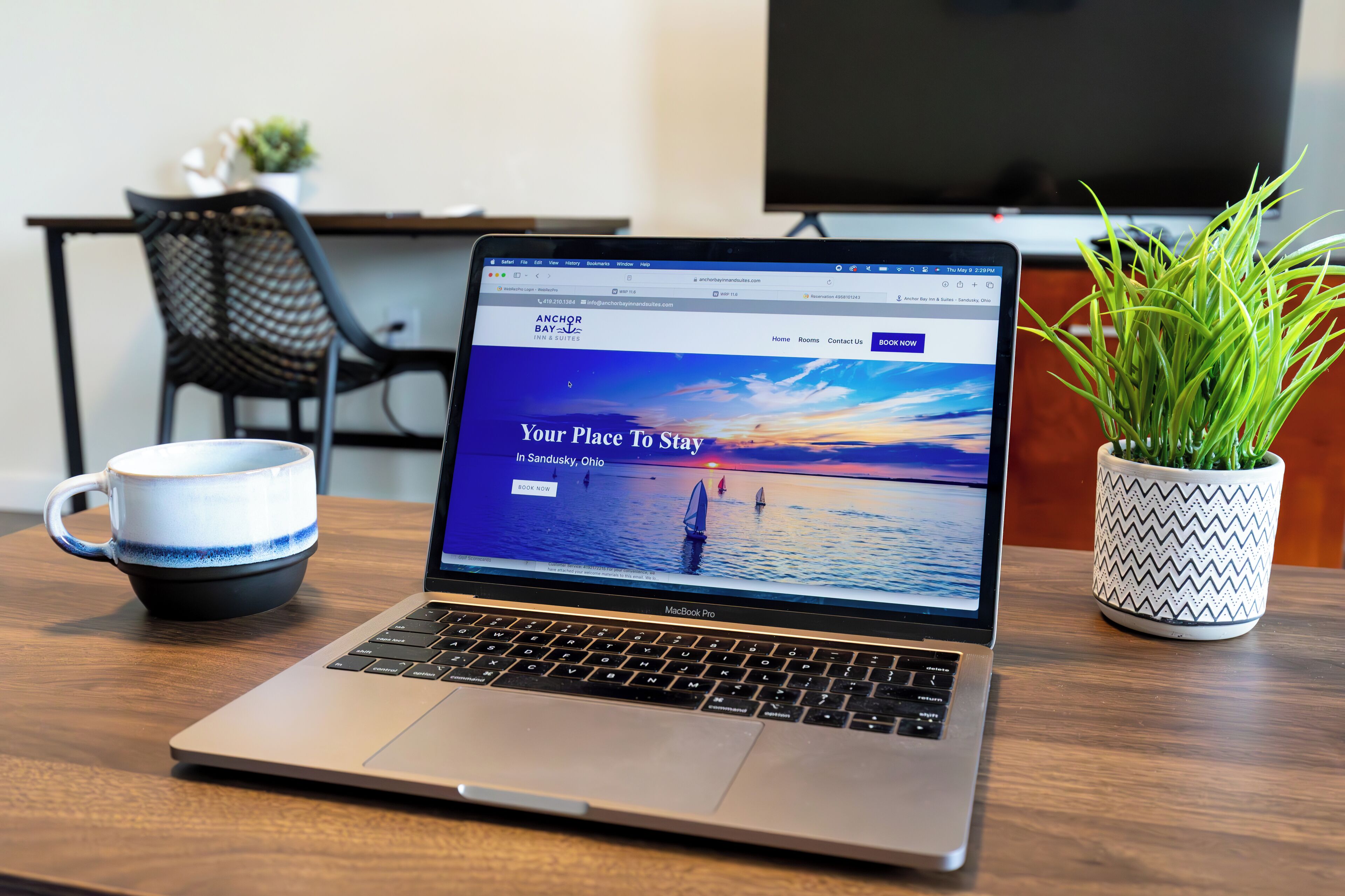 A laptop on a wooden table displaying a hotel website with a scenic view of a sunset over water.