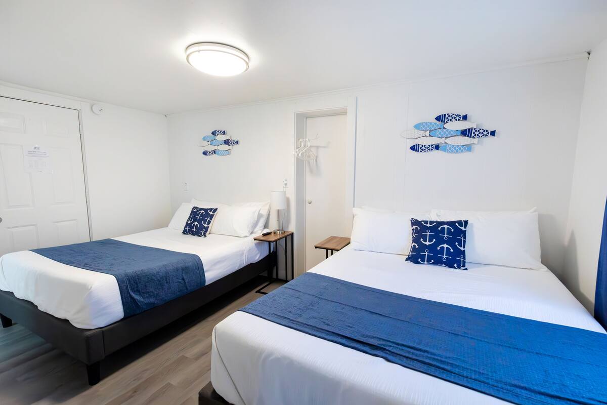 Two single beds with blue and white bedding, a small bedside table, and a wall decoration of fish.