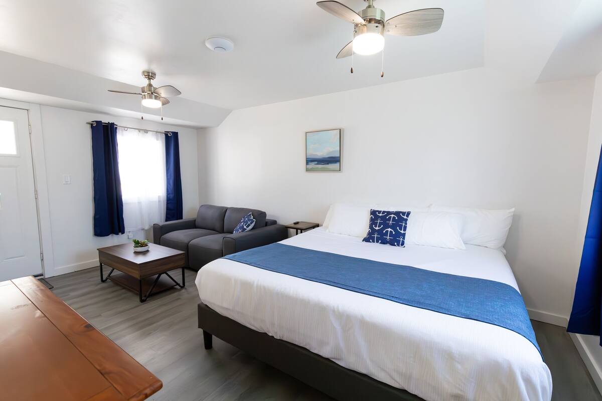 A bedroom with a bed, a desk, a chair, a ceiling fan, and a window with curtains.