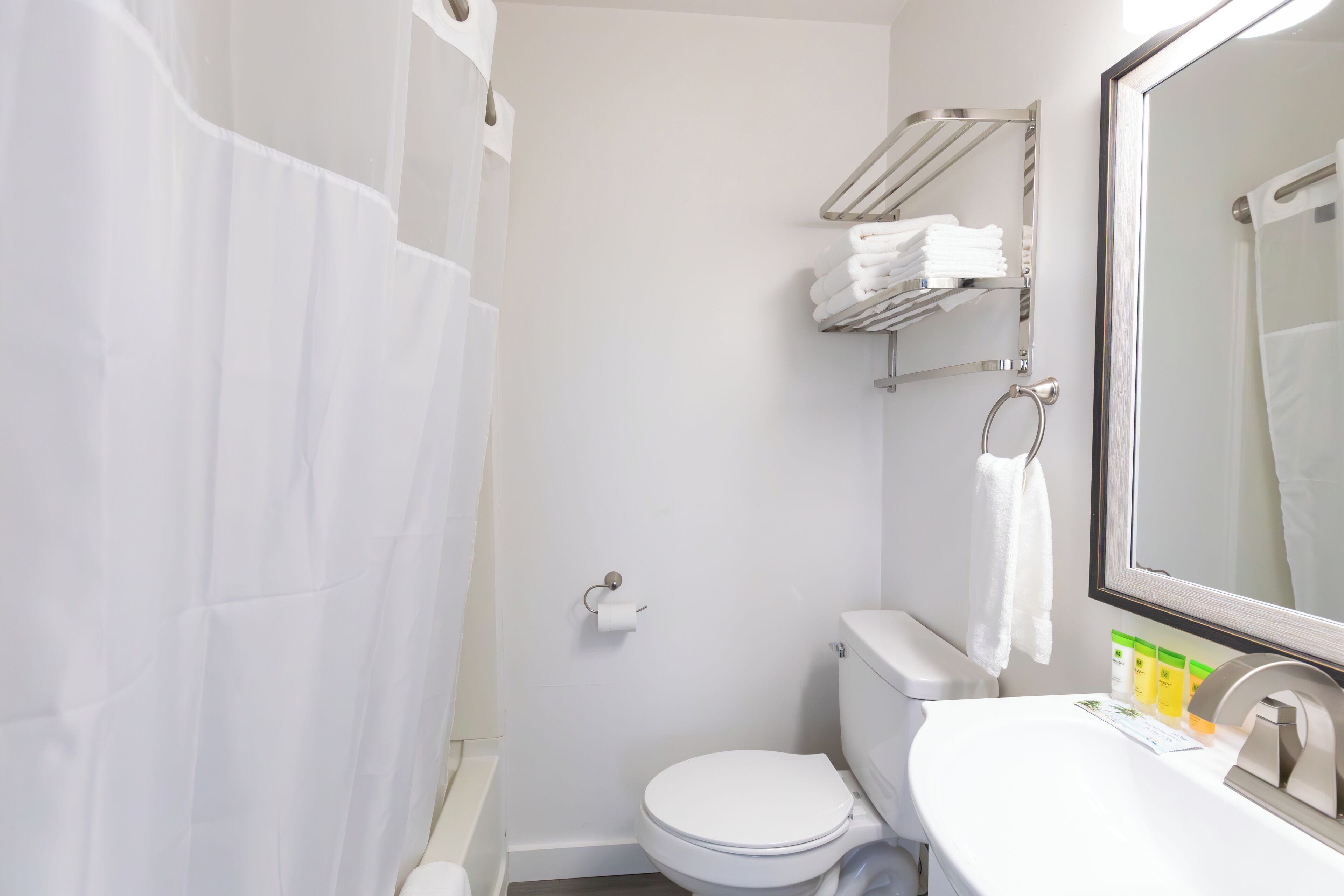 Een badkamer met een wit toilet, een wastafel met toiletartikelen, een douchegordijn en een handdoekrek met opgevouwen handdoeken.