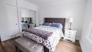 A bedroom with a bed, a bench, a nightstand, a lamp, and a wardrobe. - Elegant, large 2 bedroom main floor apartment (Toronto)