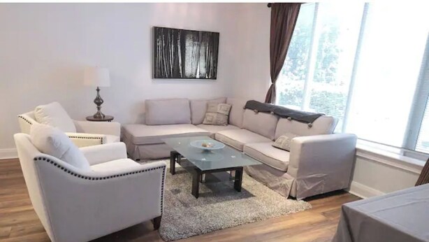 A modern living room with a sectional sofa, a glass coffee table, and a lamp. - Elegant, large 2 bedroom main floor apartment (Toronto)