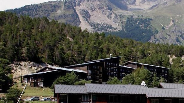 Et fjeldhotel med flere hytter, omgivet af tæt skov og bjerge.