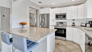 Una cocina moderna con armarios blancos, electrodomésticos de acero inoxidable, una encimera de granito y una isla integrada con taburetes de bar.