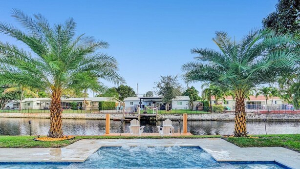 Una piscina con dos palmeras, un muelle y casas al fondo.