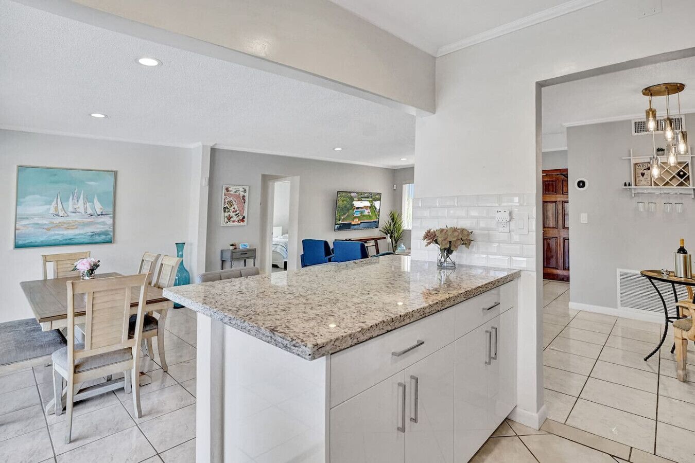 A modern kitchen with a large island, white cabinetry, and a dining area with a table and chairs.