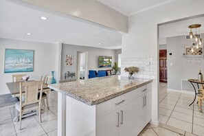 Una cocina moderna con una isla grande, armarios blancos y un comedor con una mesa y sillas.