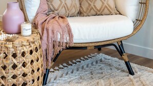 A wicker chair with cushions, a pink vase, and a candle on a woven stool. - Promenade | 3BR | BBQ, Fire Pit | Near the Beach!! (Sylvan Lake)