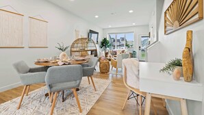 A modern living room with a dining area, featuring a round table, grey chairs, a white console table, and a large window. - Promenade | 3BR | BBQ, Fire Pit | Near the Beach!! (Sylvan Lake)