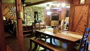 Un coin repas rustique avec une table et des bancs en bois, un mur en pierre et un poêle d’époque.