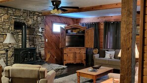 Un salon chaleureux avec un mur en pierre, des poutres en bois, une cheminée, un téléviseur et un canapé.