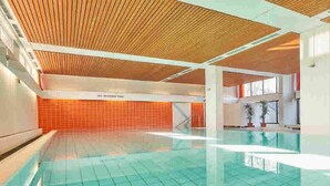An indoor swimming pool with a tiled floor and a wooden ceiling. - Ostseeperle Modernly furnished with swimming pool  (Dahme)