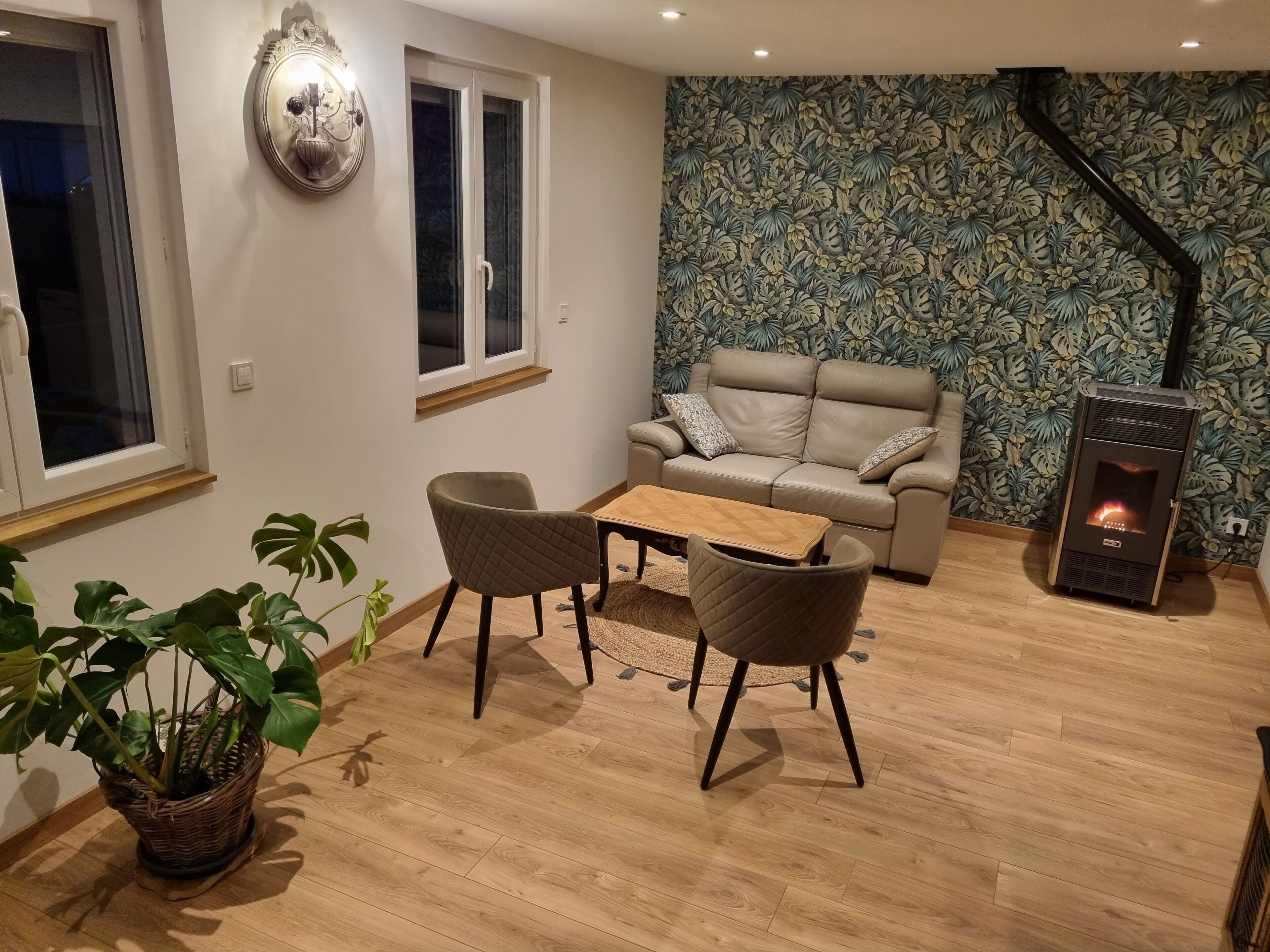 A cozy living room with a sofa, two armchairs, a coffee table, a fireplace, and a large plant.