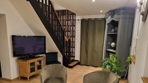 A living room with a TV, two chairs, a wooden cabinet, a staircase with bookshelves, and a large plant. - Near Châteaux & zoo de beauval: Gîte de sologne (Pruniers-en-Sologne)