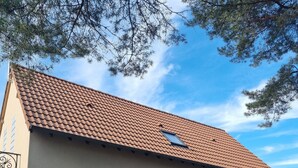 A two-story building with a tiled roof, a garage door, and a patio area with outdoor furniture. - Near Châteaux & zoo de beauval: Gîte de sologne (Pruniers-en-Sologne)
