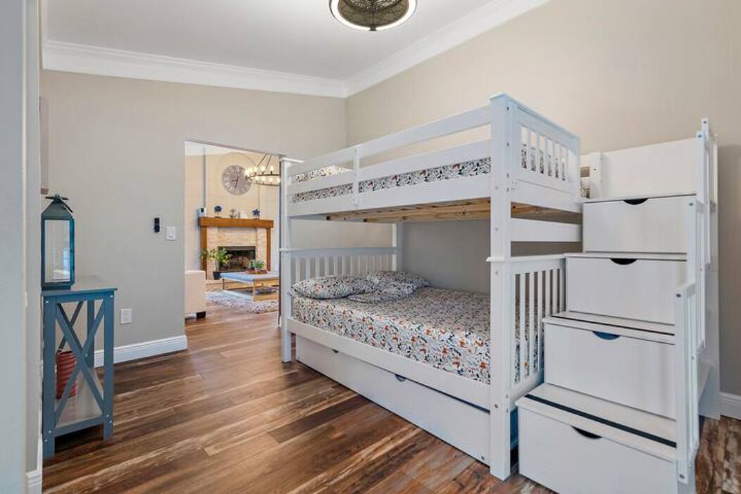 A bunk bed room with a wooden floor, a small table, and a dresser.