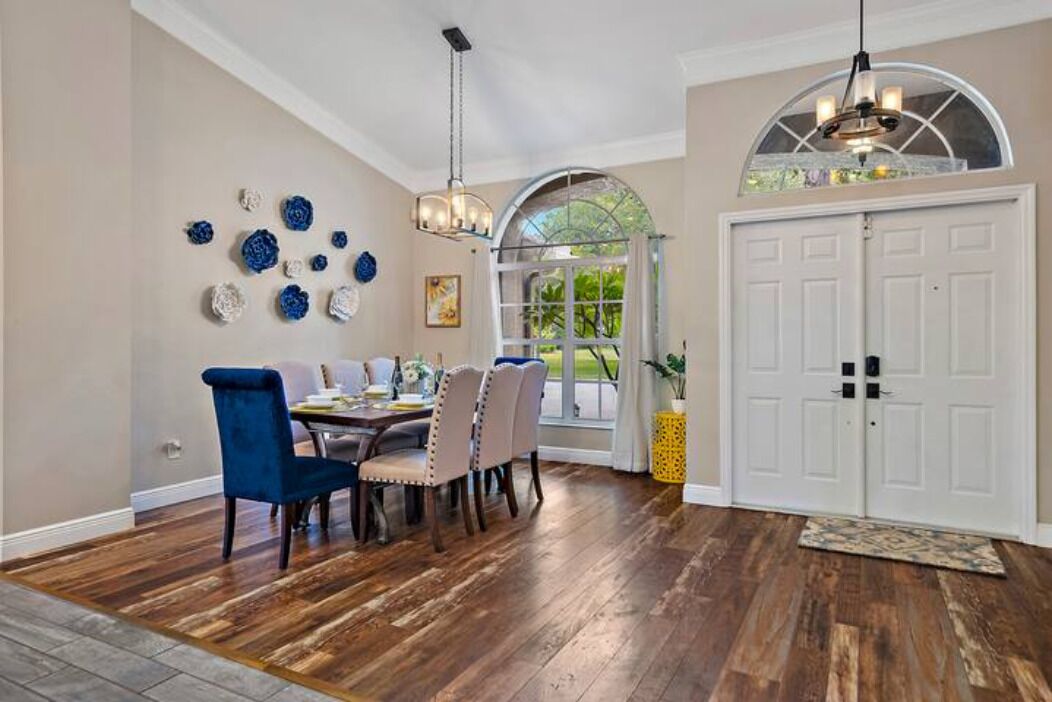 A dining area with a wooden floor, a dining table with chairs, a chandelier, and a white door with a window above it.