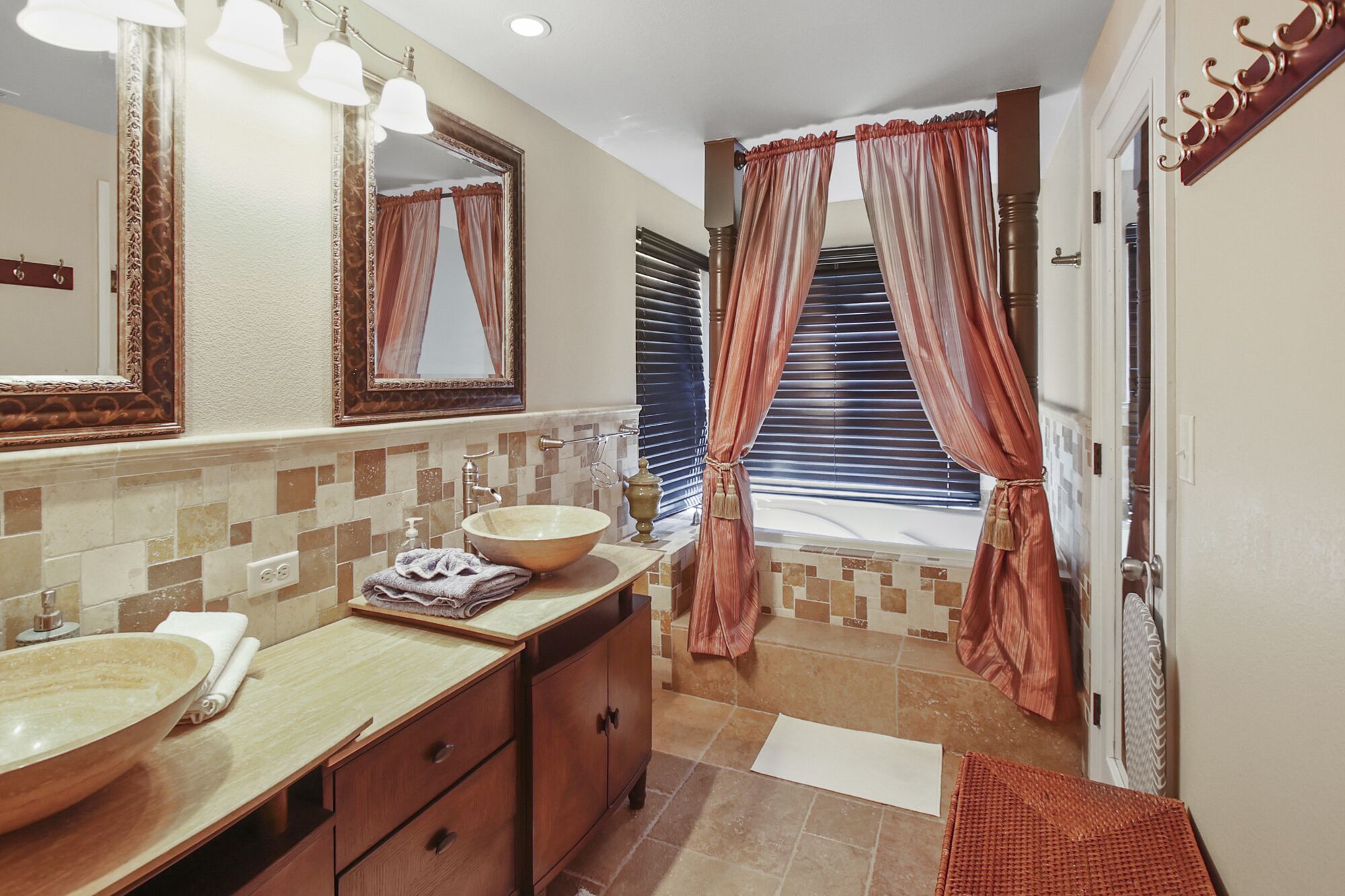 Un baño con un espejo grande, un tocador de madera, un lavabo y una ventana con cortinas.