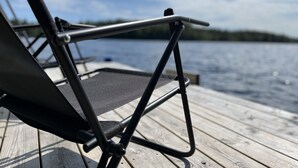 A foldable chair on a wooden deck with a view of a lake and distant shoreline. - Cozy Tiny Houseboat in the Nature (Hjulvhult)
