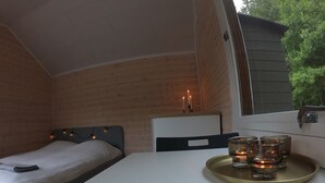 A cozy room with a bed, a small table with glasses and candles, and a window overlooking greenery. - Cozy Tiny Houseboat in the Nature (Hjulvhult)